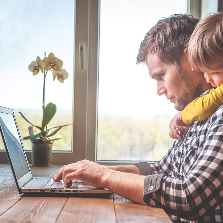 Dad working on laptop with child's arms wrapped around him