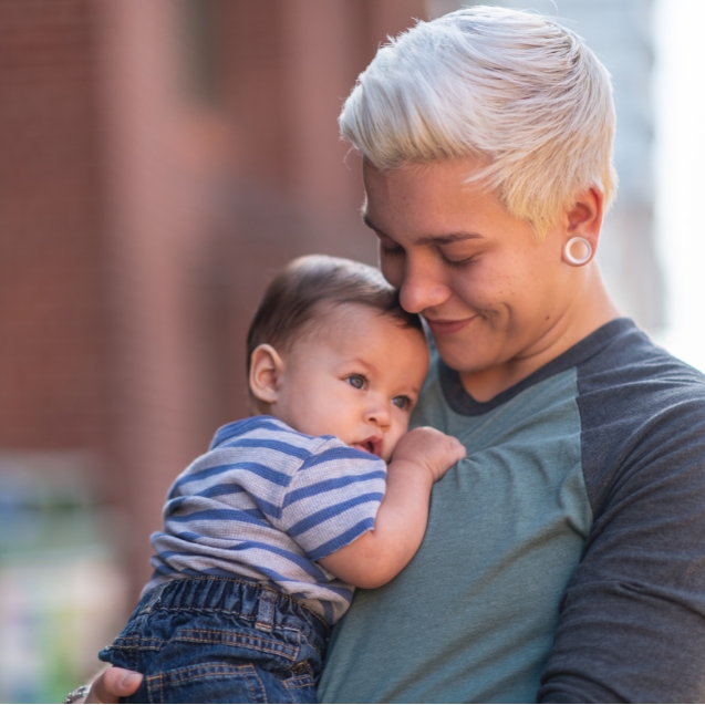 A non binary person holding their baby 