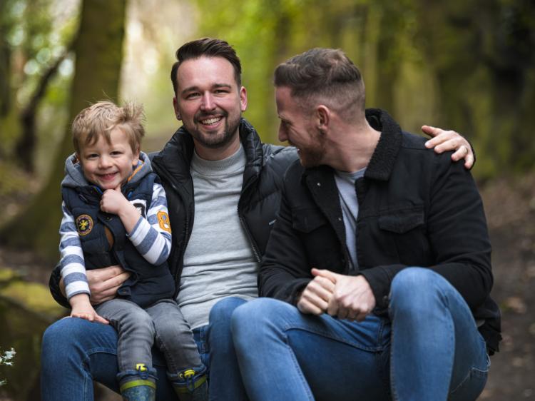 happy male couple with young son on knee in woods