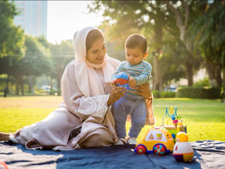 Muslim mum with toddler son playing outside with toys in a sunny park