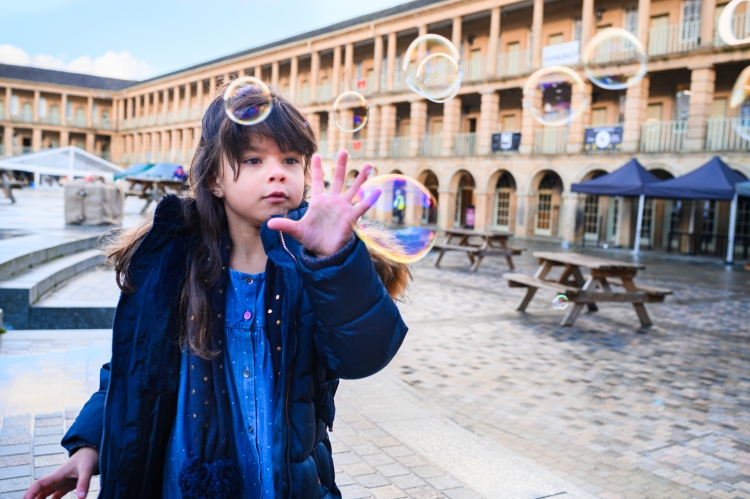 Little girl with brown hair hand outstretched looking at bubbles around her