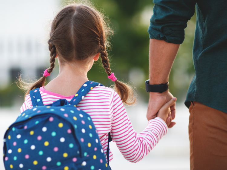 rear view of a girl with pig tail plaits with a backpack on and holding hands with a man