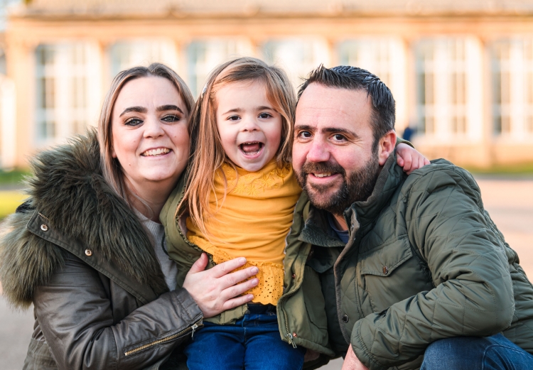little girl wearing yellow in the middle of mum and dad all smiling