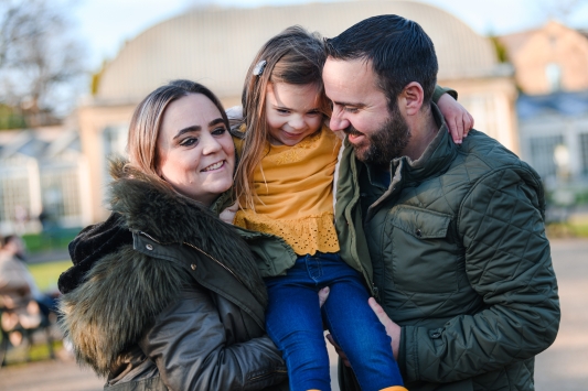 mum and dad holding up little girl in yellow top between them all smiling