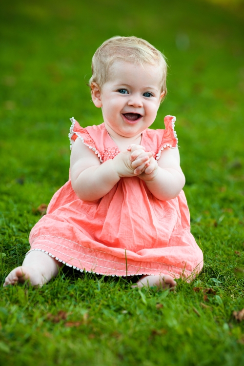 Happy baby girl laughing and clapping whilst sitting on grass